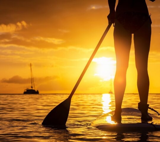 Silhouette of a person standing on a paddleboard with a paddle during a golden sunset on the ocean.