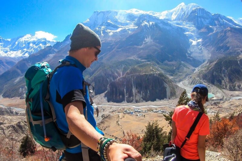 Two hikers overlooking a deep valley and massive snow-covered mountains.