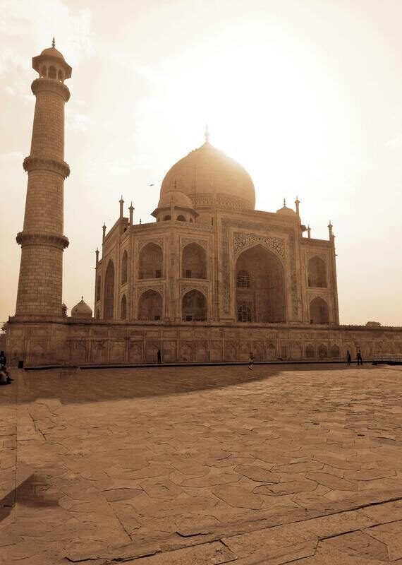 Sepia view of the Taj Mahal with a minaret on the left under a bright sky.