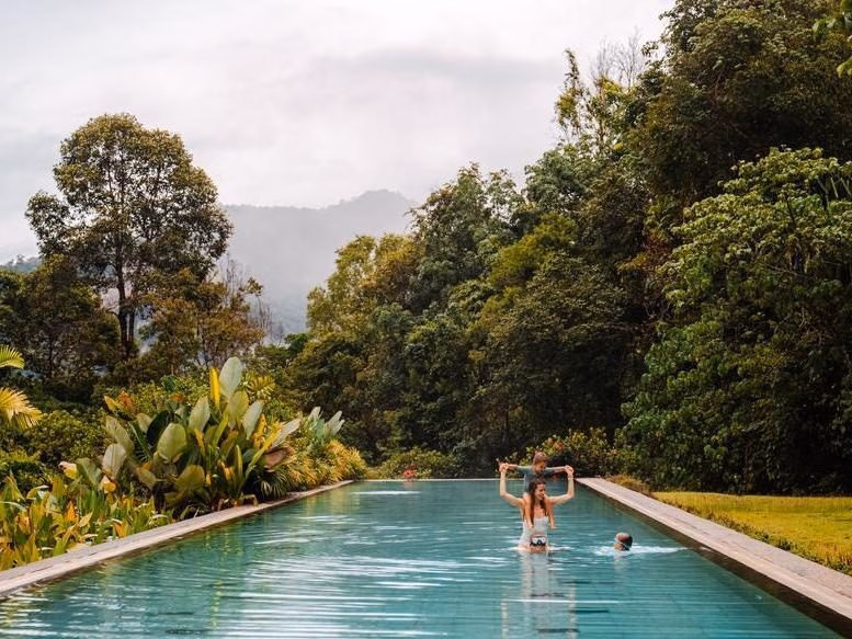 A family in a swimming pool at a resort in Thailand with Khao Sok's rolling hills in the background.