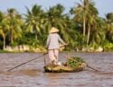 A local in traditional Vietnamese dress rowing their boat, laded with produce, down the Mekong River, Vietnam