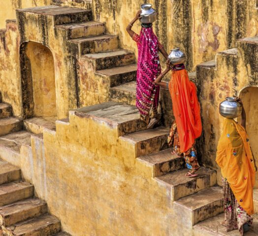 Three women in brightly coloured saris carrying water up the steps of a stepwell