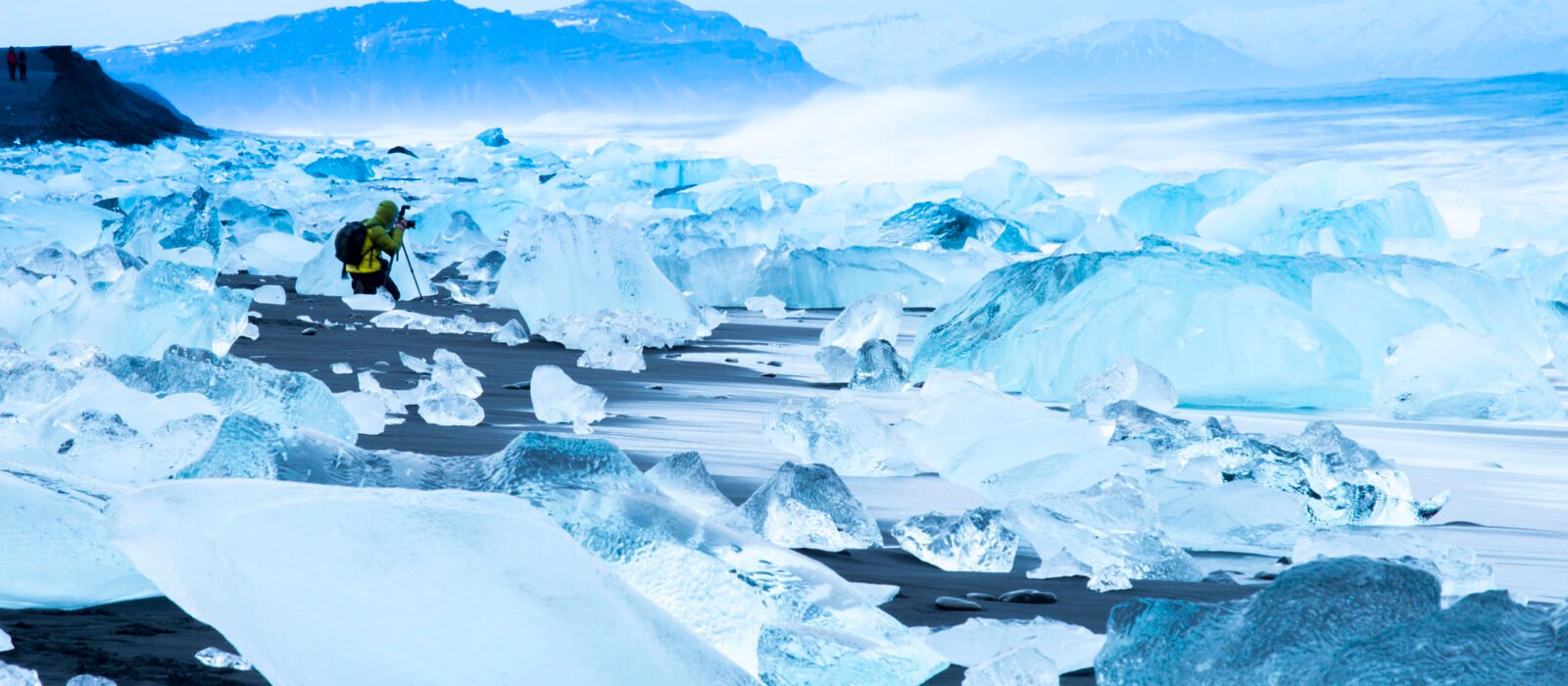 Traveller photographing broken ice which has washed up on the shore of Jokulsarlon Ice Beach, Iceland