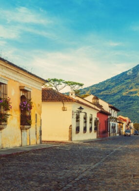 Cobblestone street of Antigua in Guatemala, lined by yellow houses with Acatenango volcano in the back