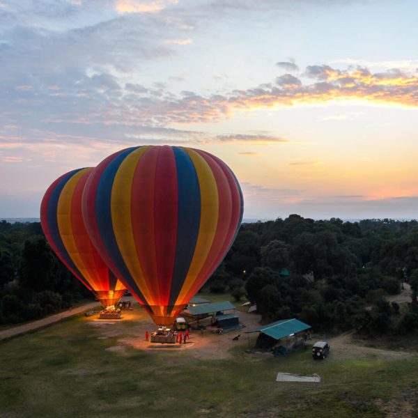 Two rainbow striped hot air balloons firing up up on the ground preparing for take off