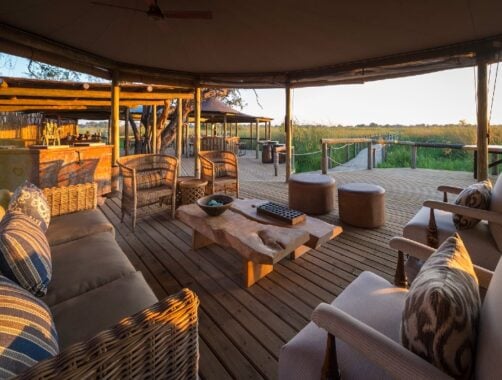 Covered outdoor seating area with sofas and armchairs around a low wooden table