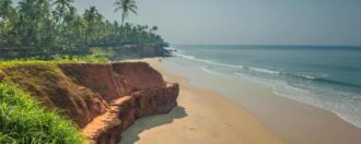 View of the golden sands of Varkala beach, Kerala, India, with palm tree forest on the hill overlooking the sea