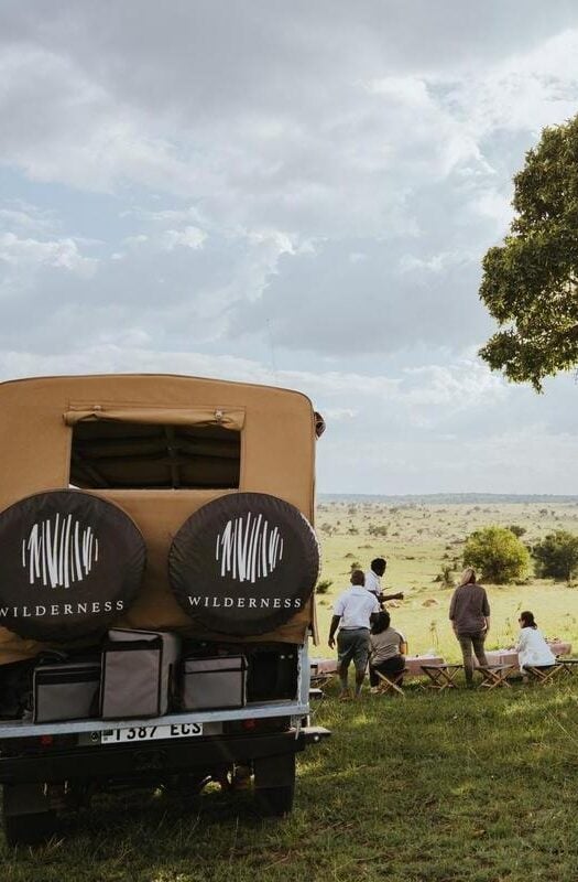 A small group of travellers and their safari guides stopping for lunch next to their safari vehicle, Serengeti National Park, Tanzania.