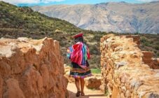 Quechua Indigenous Woman in traditional clothes walking along ancient Inca Wall