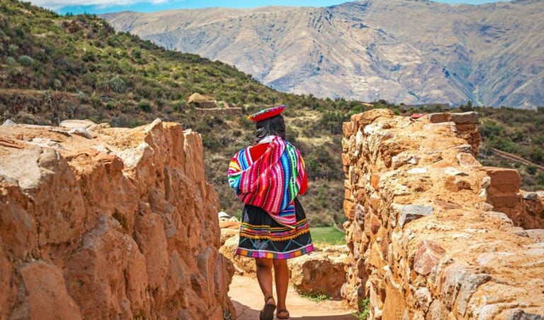 Quechua Indigenous Woman in traditional clothes walking along ancient Inca Wall