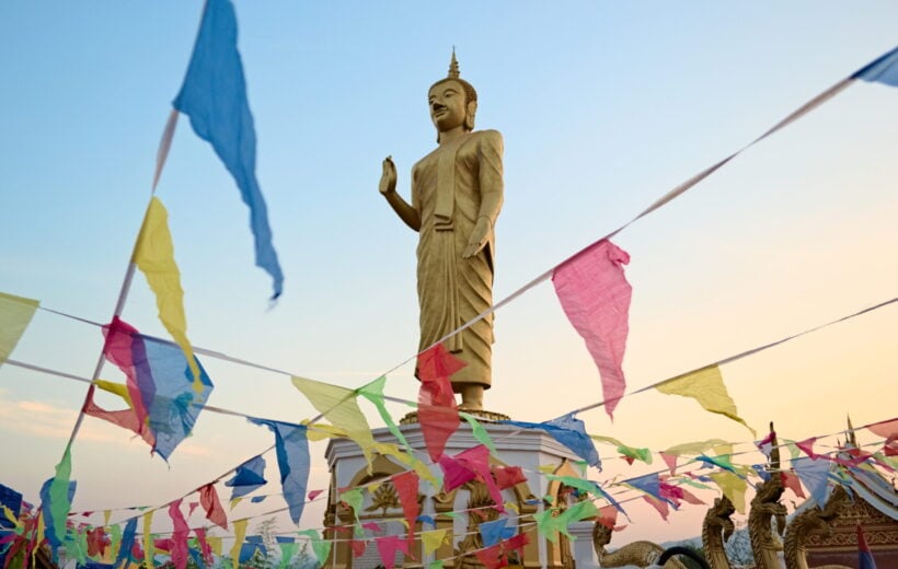 A golden religious statue surrounded by colourful flags in Oudomxay, Laos