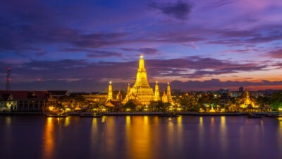 Bangkok's Wat Arun temple at night, glowing golden against a purple sky