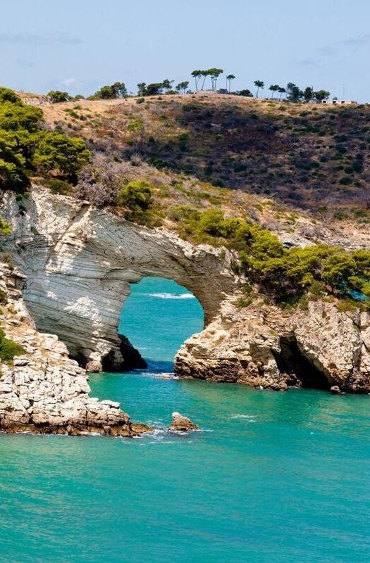 Gargano national park in Puglia, Italy, with a dramatic rock archway eroded out of the coastline through which bright blue sea is visible