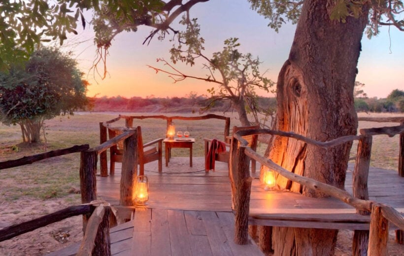 Outdoor seating area lit by glowing lanterns, with two chairs and a small table with wine glasses