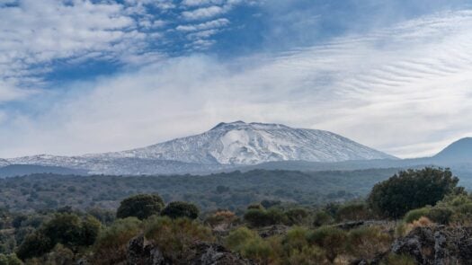 A view of a snow-covered Mount Etna and the wild hills of the Sicilian backcountry