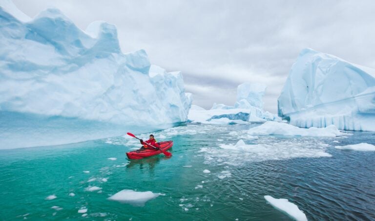 man paddling on kayak between ice in Antractica in Iceberg Graveyard, extreme winter kayaking, polar adventure near Pleneau island