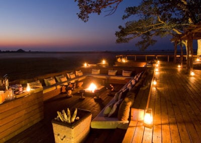 Exterior image of outdoor seating area on a wooden verandah. Comfy chairs around fire pits with softly glowing lanterns