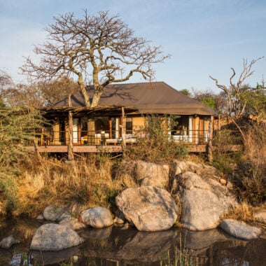 External shot of suite at Mwiba Lodge, a building with outdoor seating area in front of a river