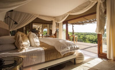 Bedroom at Mwiba Lodge, decorated in a safari style with neutral colours, and a large bed with a view of the African landscape