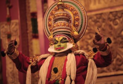 A dancer in traditional clothing, mask, and headdress dances on stage