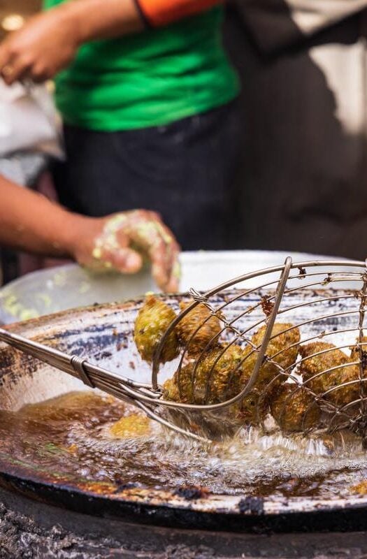 A vendor frying falafel balls in the street