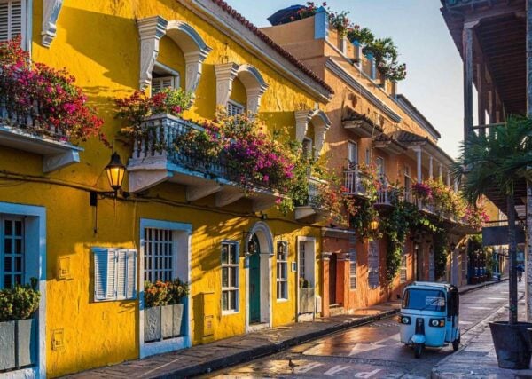 A beautiful street with bright yellow Colonial-style buildings and a motorised tuk tuk on the road in Cartagena, Colombia