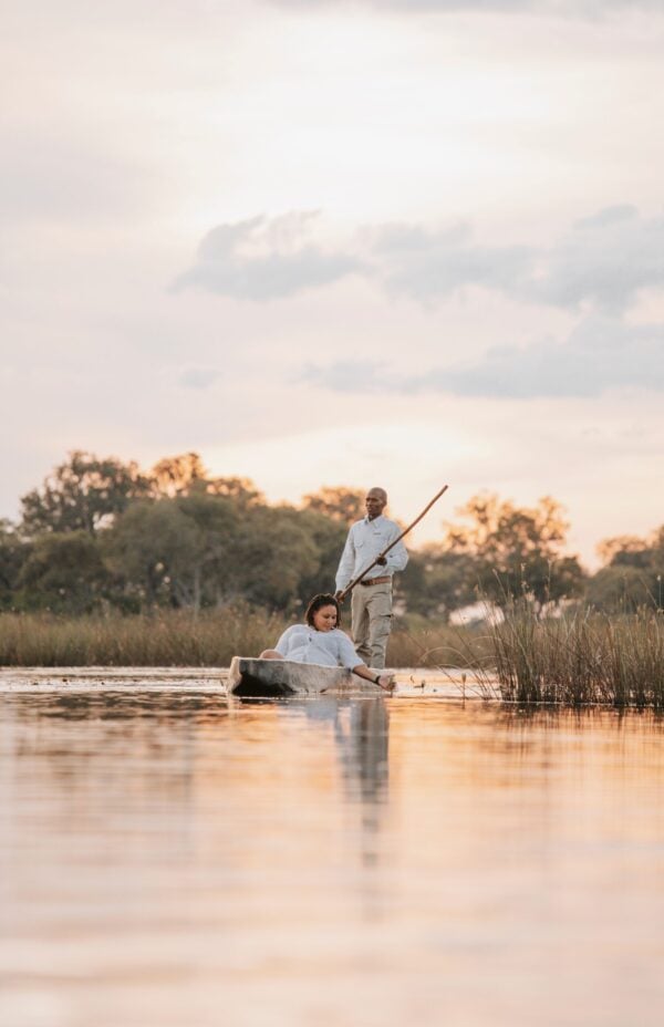 A man stands on small boat rowing a seated woman through calm waters