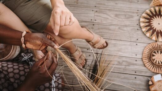 Close up of two people weaving traditional mats with grass reeds