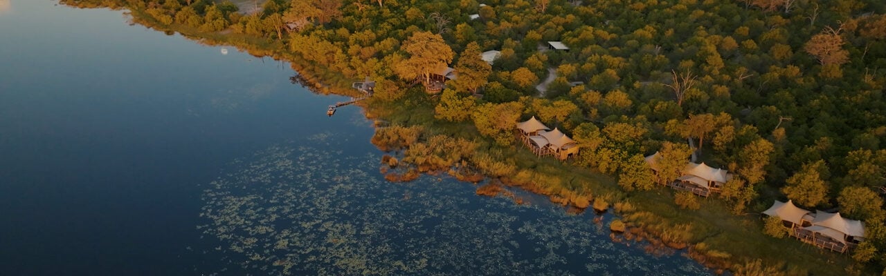 Aerial image of luxury safari camp villas on the edge of water surrounded by trees and vegetation