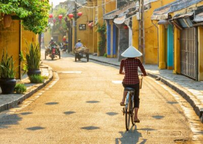 Vietnamese woman in traditional hat bicycling along in Hoi An