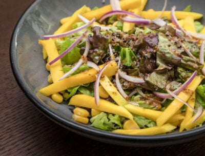 Close up of bowl of salad with lettuce, corn, red onion, and mustard seeds