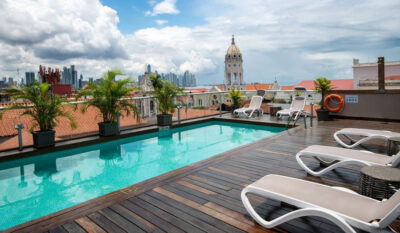 View of the city skyline from a rooftop area with pool an d deckchairs