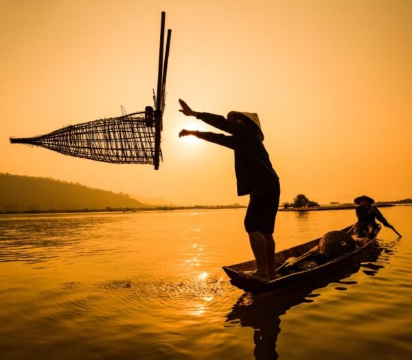 Fisherman on boat river sunset / Asia fisherman bamboo fish trap on wooden boat sunset or sunrise in the Mekong river - Silhouette fisherman boat with mountain background life person countryside