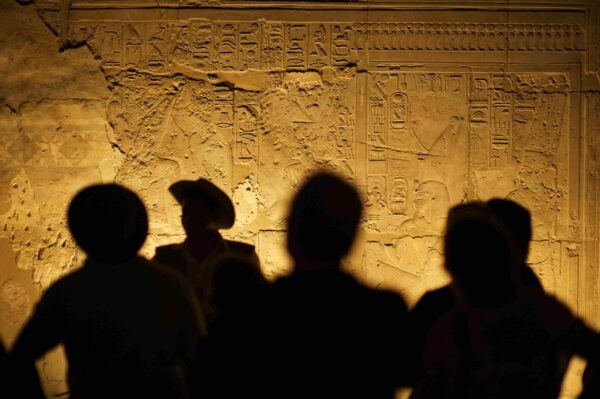 Group of unrecognizable tourist archeologists standing in silhouette in front of ancient Egyptian hieroglyphs