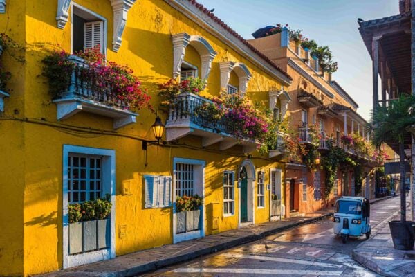 A beautiful street with bright yellow Colonial-style buildings and a motorised tuk tuk on the road in Cartagena, Colombia