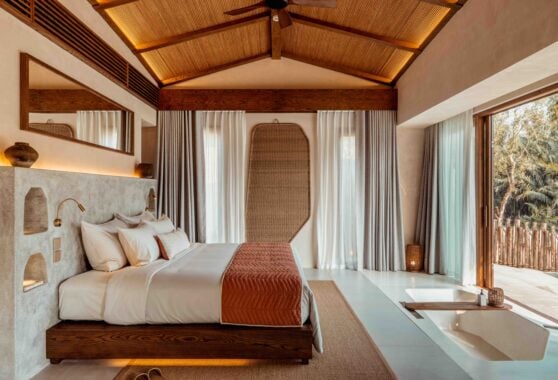 Bedroom in a villa with large double bed with cream and burnt orange bedding, and a bath sunken into the4 floor at the foot of the bed