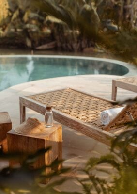 A wooden sun lounger by a private pool with a small wooden table