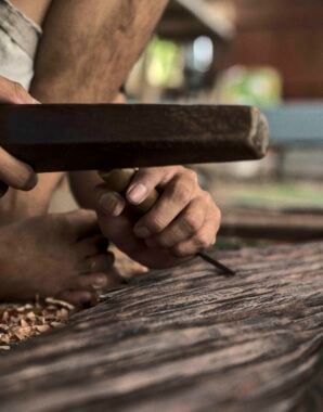 Close up of hands working on a wooden carving using traditional tools