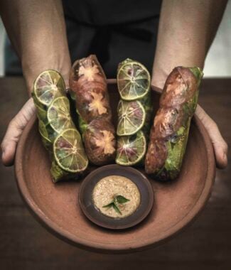 Close up of hands holding out a terracotta bowl with leaf-wrapped food