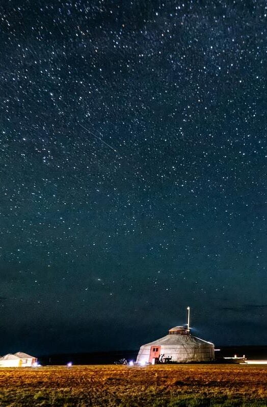 Mongolia camp at night, with many stars visible in the clear night sky and a meteor streaking through the stars.