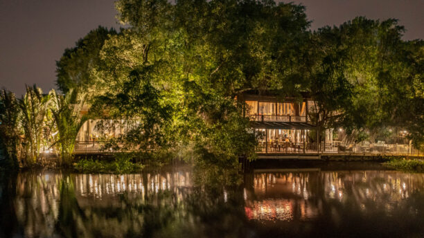 Exterior night shot of hotel by a river with large trees