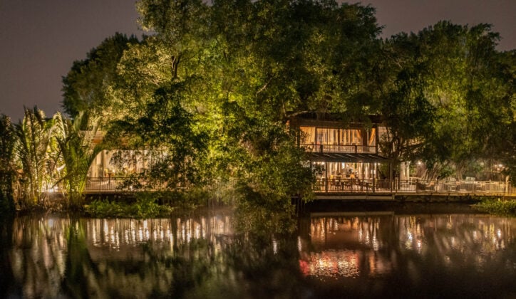 Exterior night shot of hotel by a river with large trees