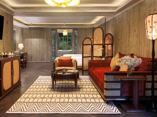 Interior view of hotel living room with large red sofa, small glass topped round table, comfy arm chair and patterned rug