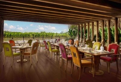 A covered dining area at a hotel with long and small tables around which colourful high-backed chairs are set