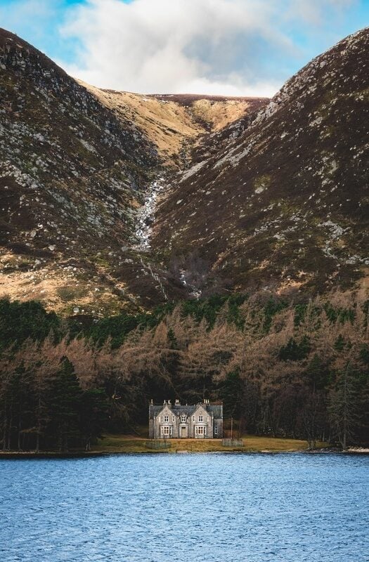 A grand house on the shores of a lake, with a pine forest behind in Loch Muick in Aberdeenshire, Scotland