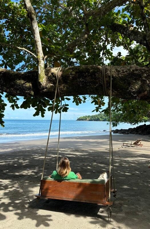 A woman sitting on a swinging bench under a large tree on Panama beaches Islas Secas