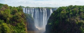 A view of the large waterfall Victoria Falls on the Zambezi River in South Africa, with many streams of water cascading down a tall cliff face in to a wide river