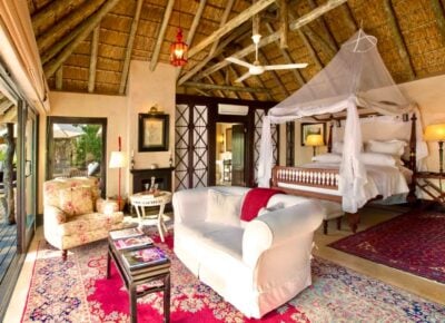 Bedroom in a tropical hotel, with four poster bed decorated with net covering, a white sofa and small coffee table laid out with books