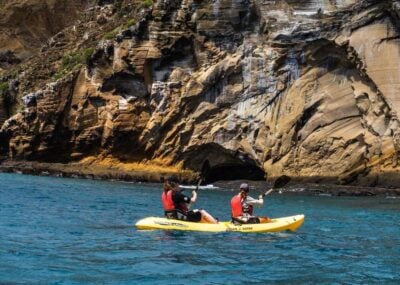 Two people sea kayaking in a yellow kayak in front of a rocky cliff face