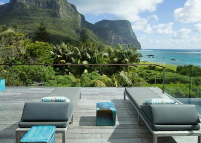 An outdoor sun terrace with two sun loungers on a wooden deck with a view of sea and mountains on Lord Howe Island